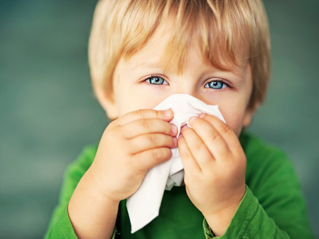 Mały, blond chłopiec smarkający w chusteczkę